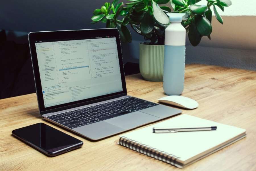 Un laptop gris ouvert affichant du code sur un bureau en bois bien organisé, illustrant comment entretenir son laptop dans un espace de travail soigné.