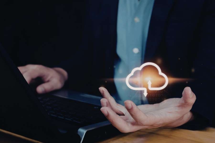 Gros plan sur un utilisateur de dos tapant sur un ordinateur avec un symbole lumineux de cloud au-dessus de sa main.