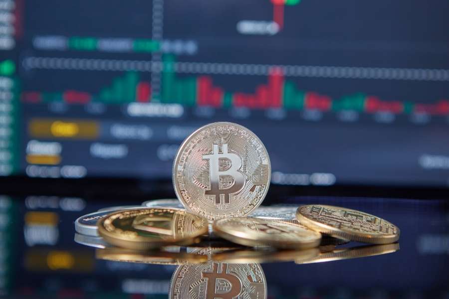 Pièce de Bitcoin dressée devant un écran de marché pour illustrer la finance décentralisée.